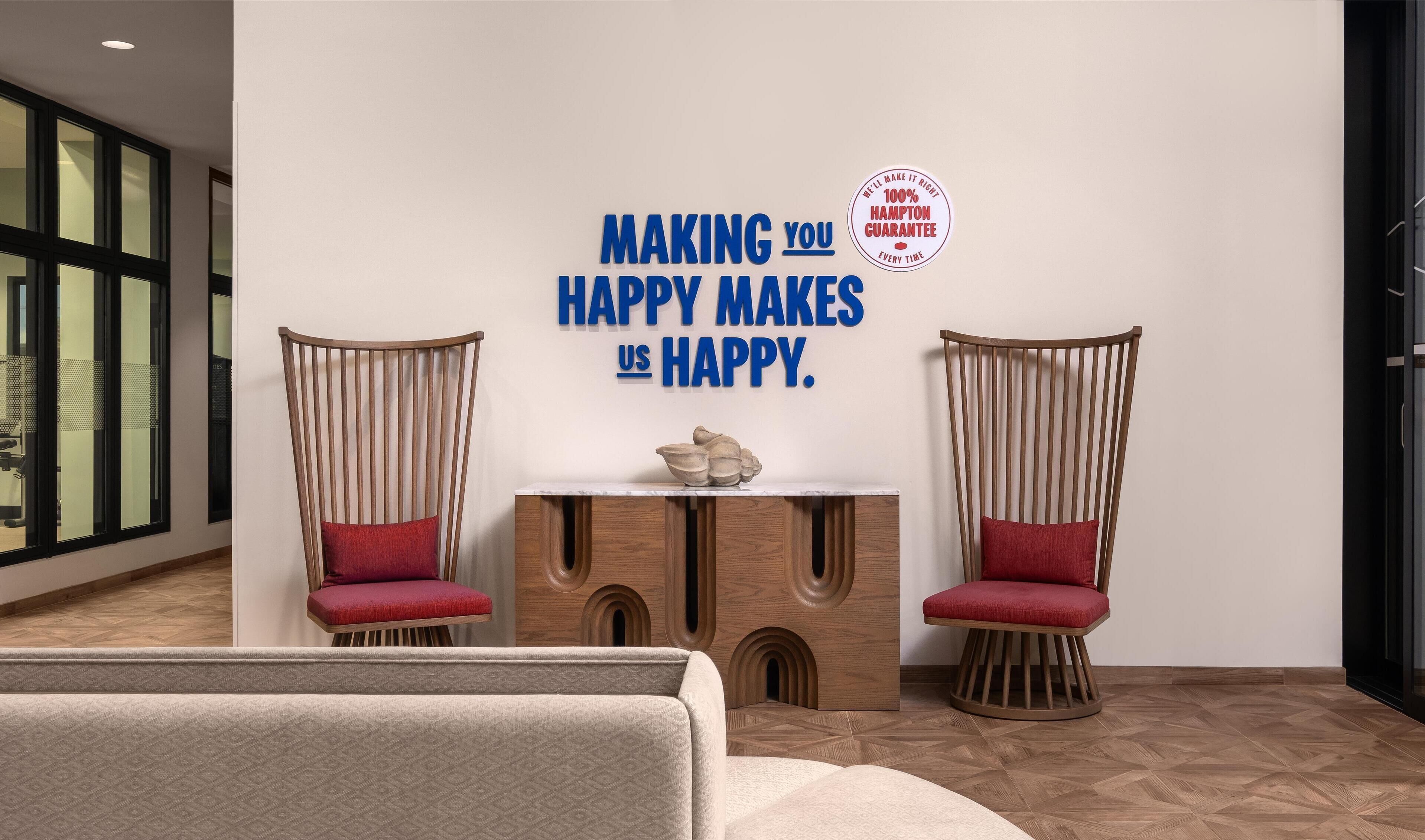 A modern interior with two wooden chairs with red cushions, a small wooden table with a decorative bowl, and a wall with a motivational quote.