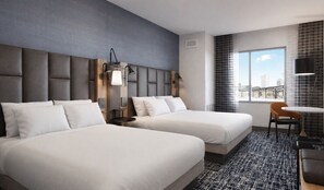 Quarto de hotel com duas camas, uma mesa pequena, uma cadeira e vista para a cidade.