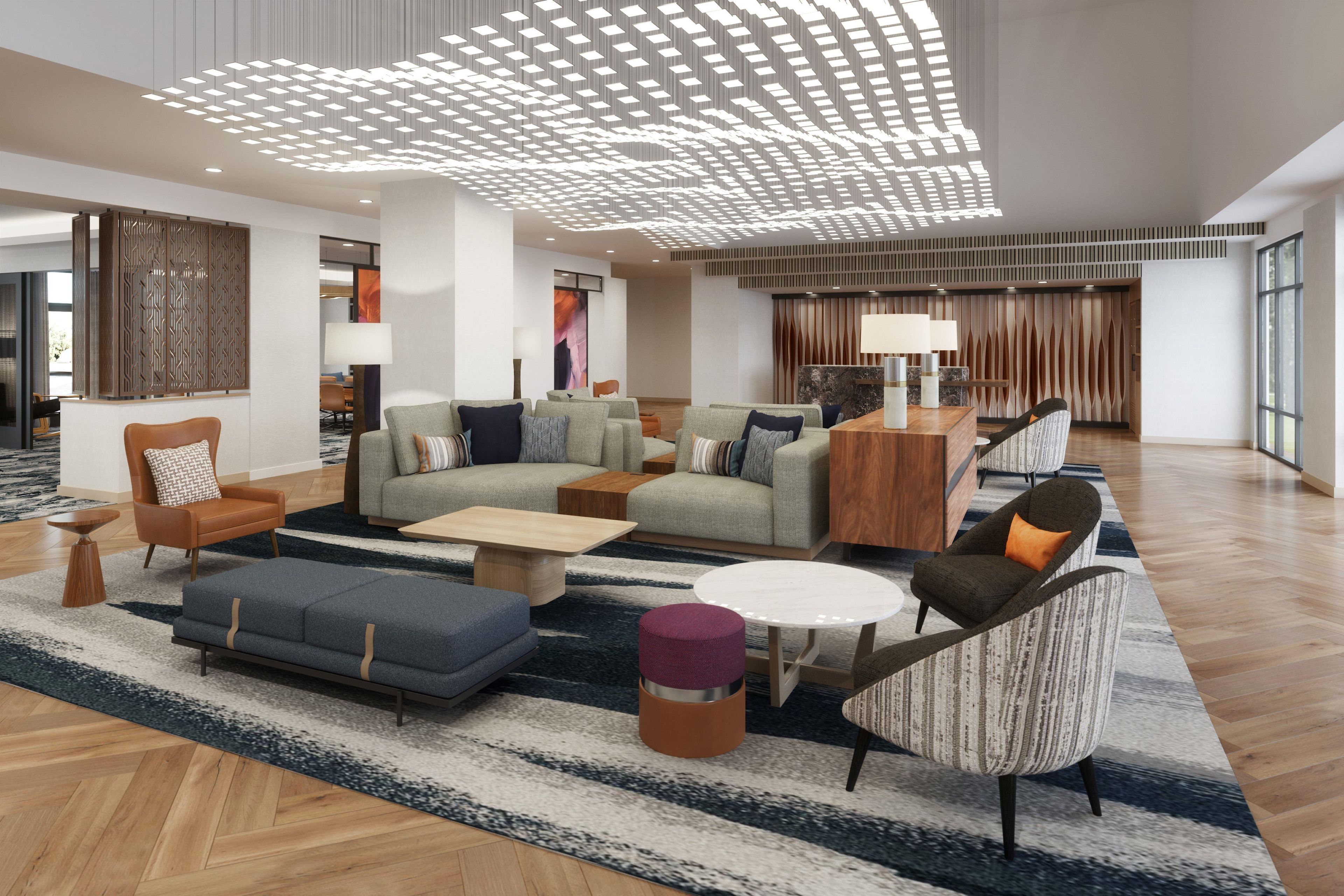 A spacious lobby with a modern design, featuring a seating area with sofas and armchairs, a coffee table, and a decorative ceiling light fixture.