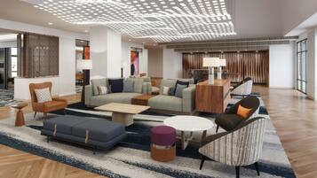A spacious lobby with a modern design, featuring a seating area with sofas and armchairs, a coffee table, and a decorative ceiling light fixture.