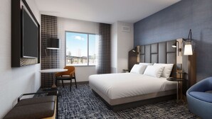 Een hotelkamer met een bed, een bureau, een stoel, een bank, een televisie en een raam met uitzicht over de stad.