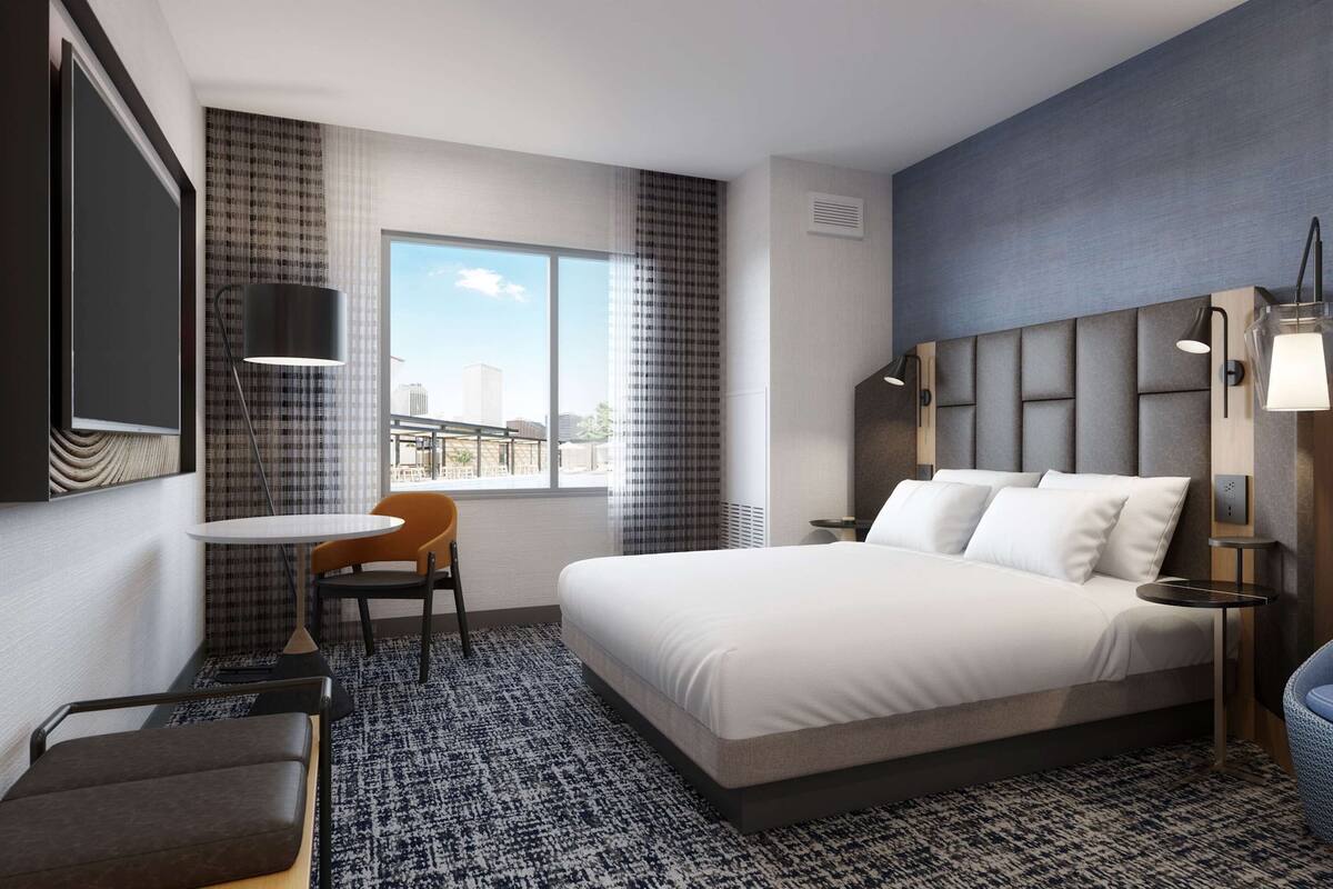 Een hotelkamer met een bed, een bureau, een stoel, een bank, een televisie en een raam met uitzicht over de stad.