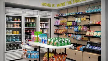 Una sección de snacks con estantes refrigerados y no refrigerados, una variedad de productos envasados, y un letrero que dice “HOME IS WHERE THE SNACKS ARE”.