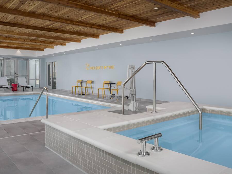 An indoor swimming pool with wooden beams on the ceiling, a tiled floor, and a wall with a sign that reads "POOLSIDE IS MY VIBE".