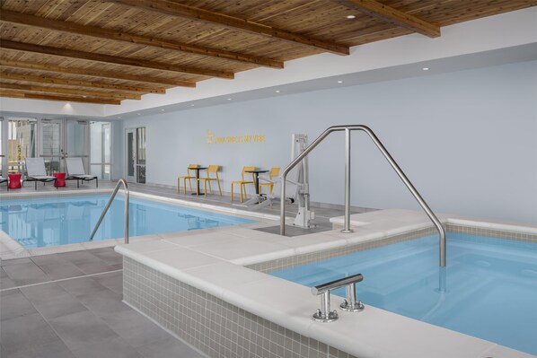 An indoor swimming pool with wooden beams on the ceiling, a tiled floor, and a wall with a sign that reads "POOLSIDE IS MY VIBE".