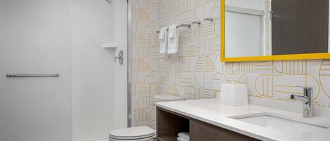 A modern bathroom with a shower, toilet, and vanity with a mirror.