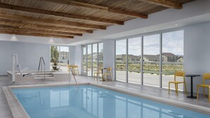 A modern indoor swimming pool with wooden beams, large windows, and yellow chairs. - Home2 Suites By Hilton Tooele (Tooele)