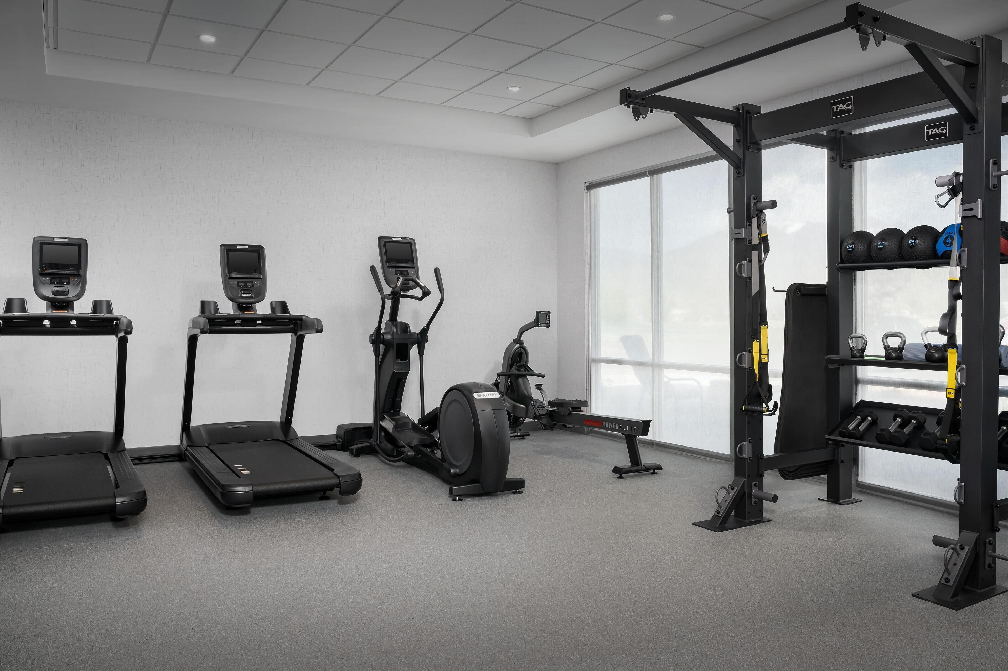 A gym with treadmills, elliptical machines, and a squat rack with weights.
