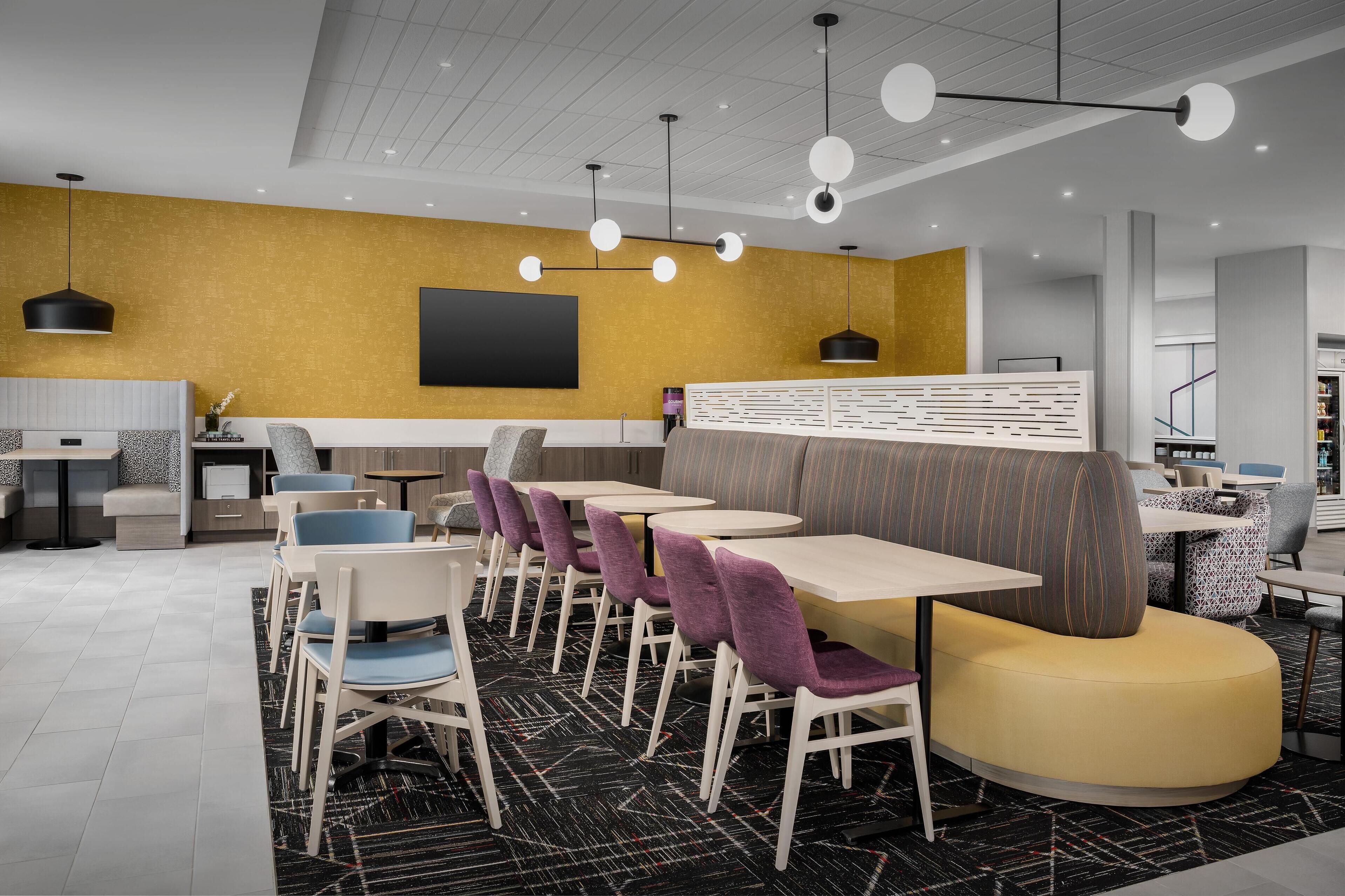 A modern dining area with round tables, purple chairs, and a yellow booth.