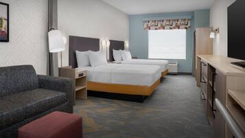 A hotel room with two beds, a sofa, a TV, and a desk.