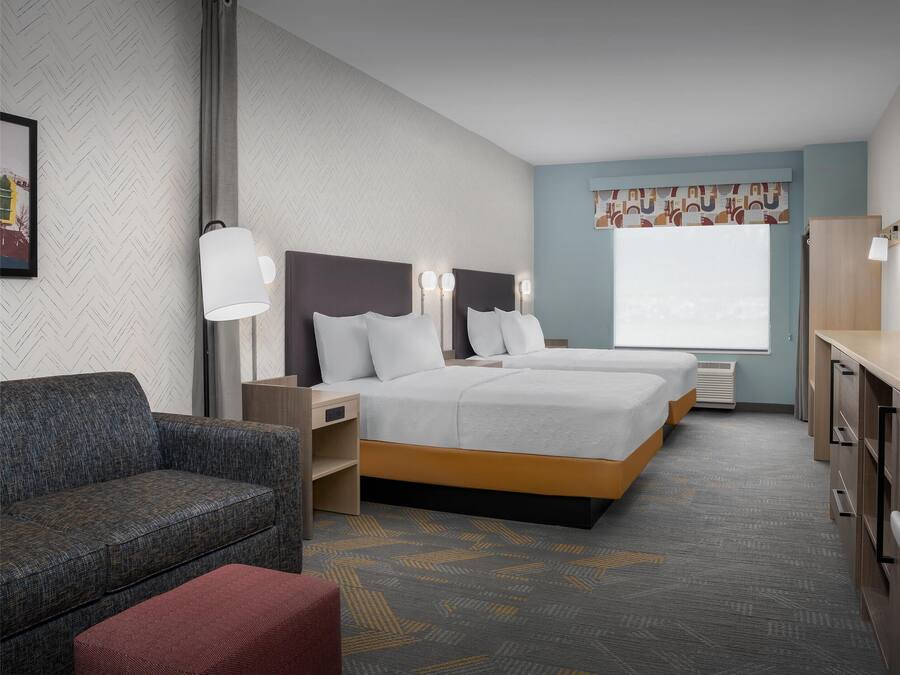 A hotel room with two beds, a sofa, a TV, and a desk.