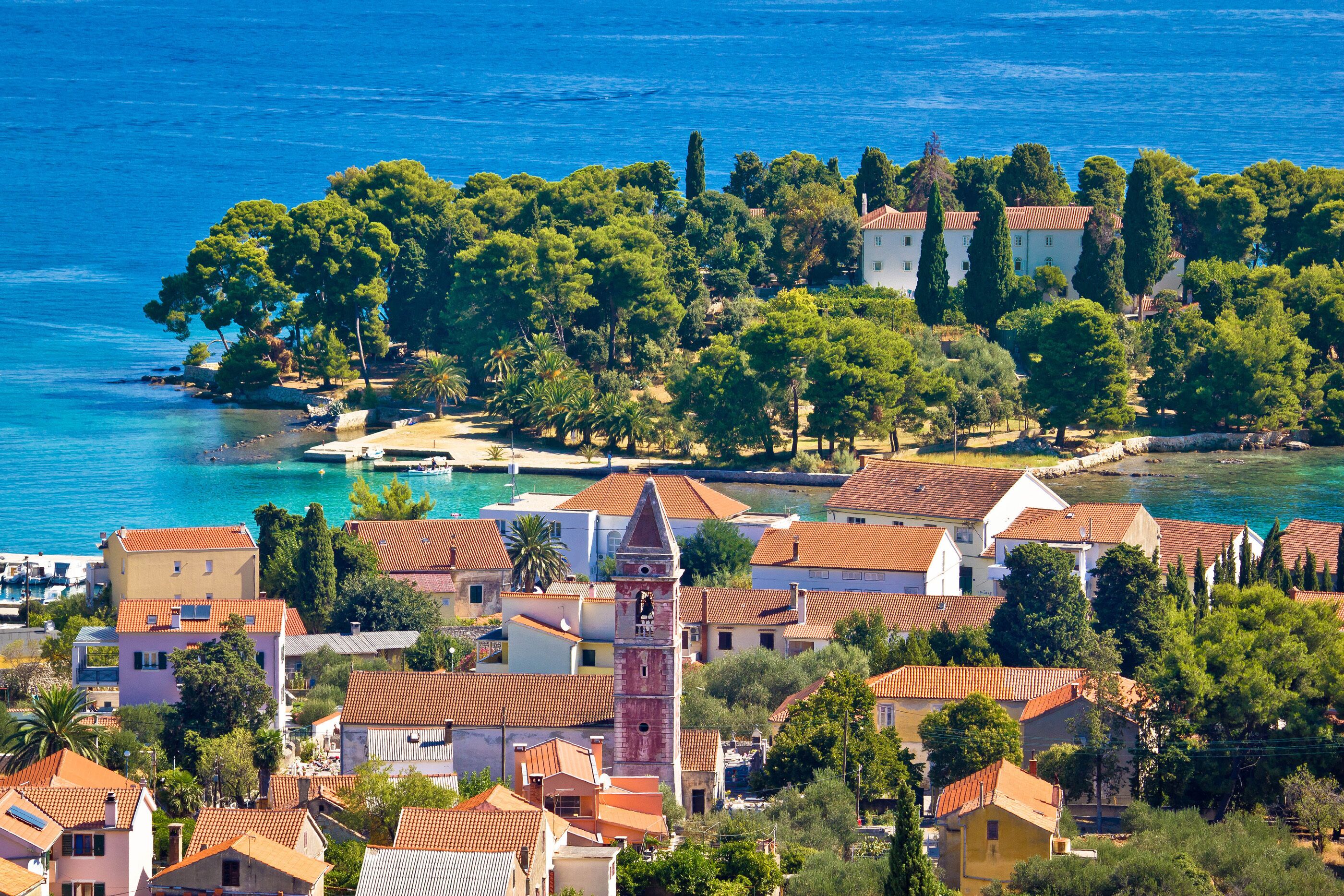 A coastal town with a prominent tower, terracotta-roofed buildings, and a clear view of the sea.