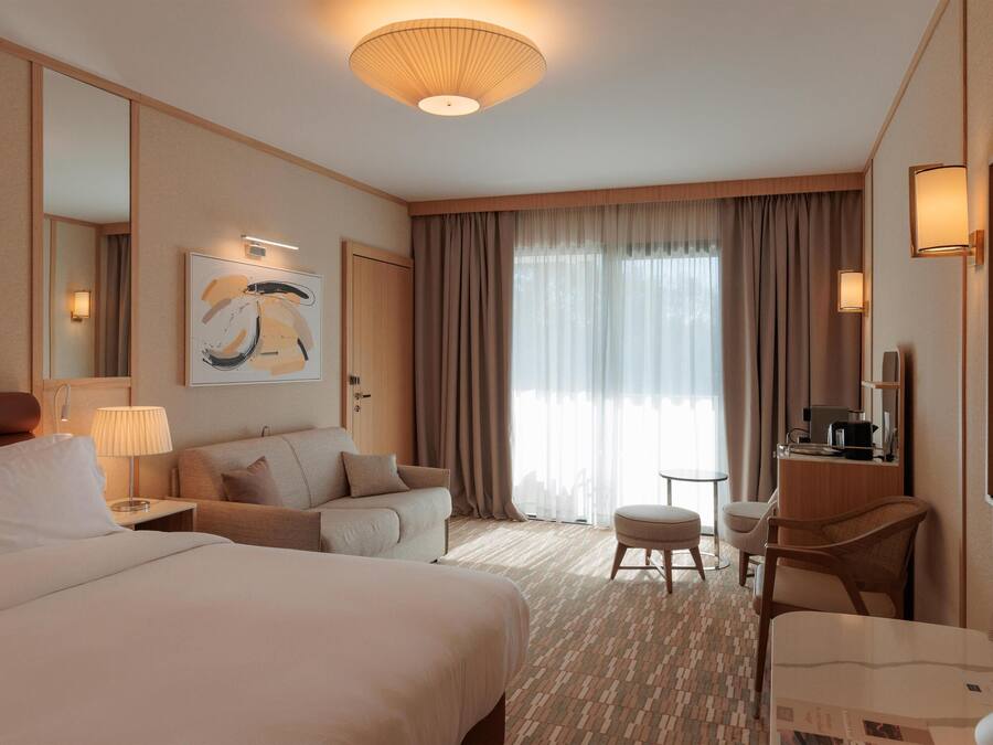 Une chambre d’hôtel avec un grand lit, un canapé, un bureau avec une chaise, une petite table et un téléviseur.