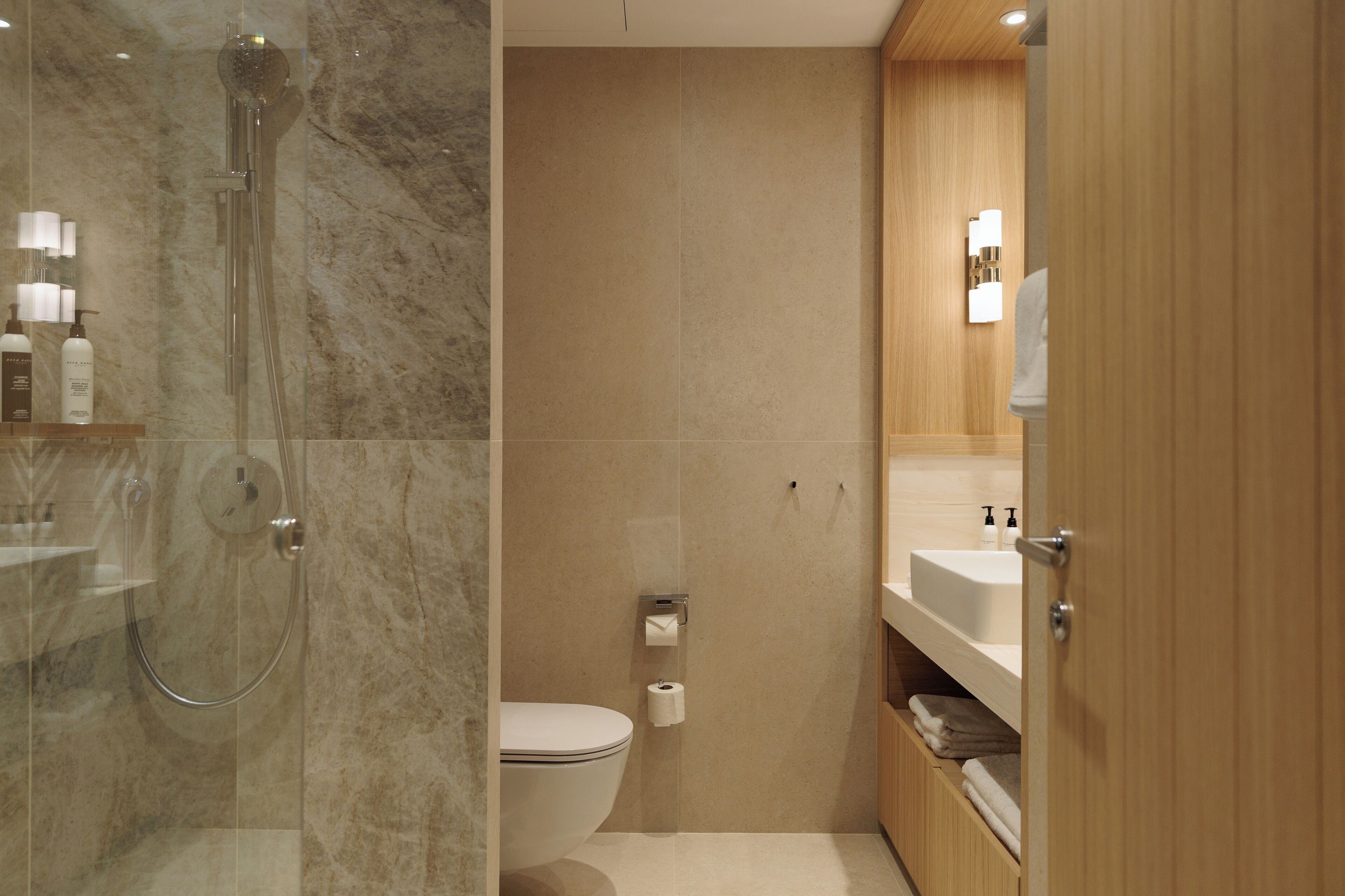 A modern bathroom with a glass-enclosed shower, a toilet, and a wooden vanity with a sink and mirror.
