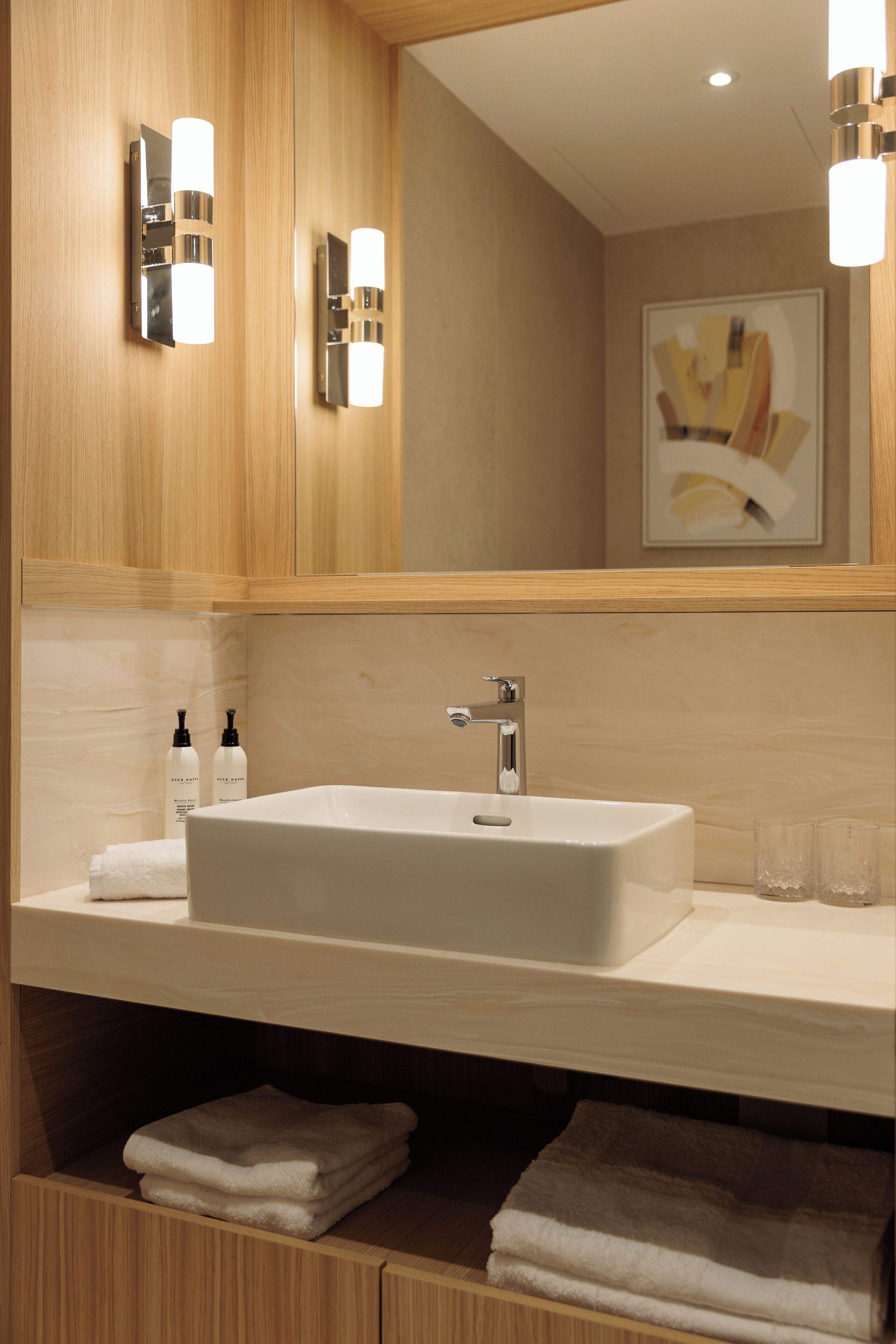 Une salle de bain moderne avec un grand miroir, un lavabo blanc et deux appliques murales.