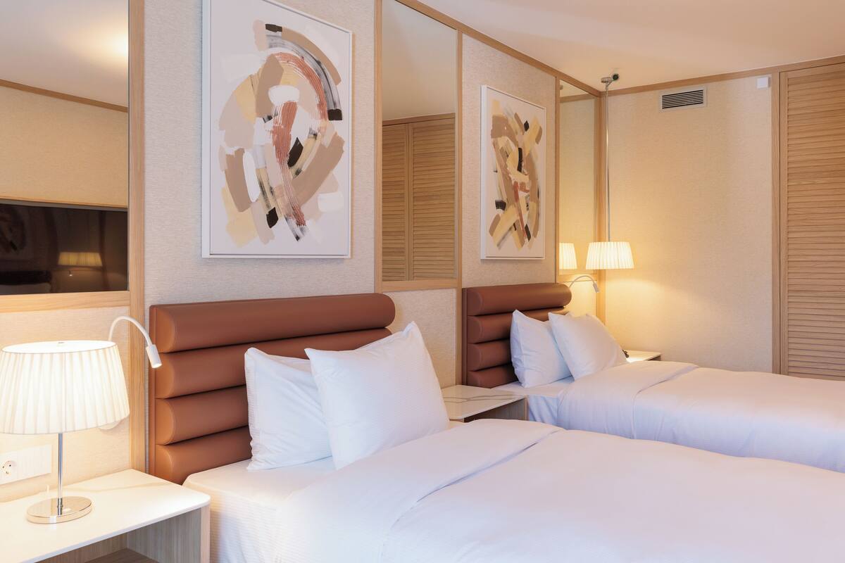 Une chambre d’hôtel avec deux lits, une table de chevet, une lampe et des œuvres d’art abstraites accrochées au mur.
