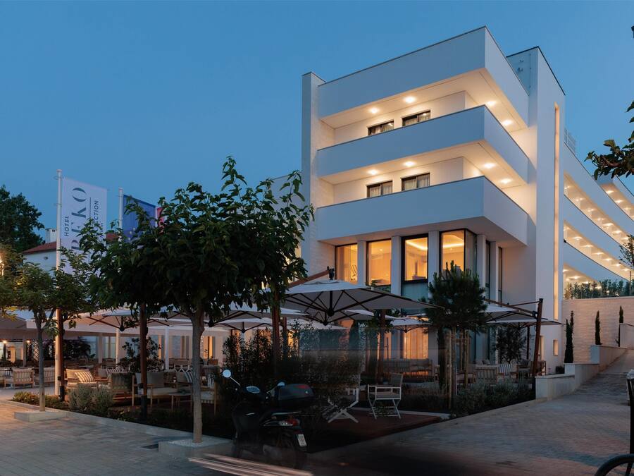 A modern hotel with multiple floors, outdoor seating, and a well-lit entrance.