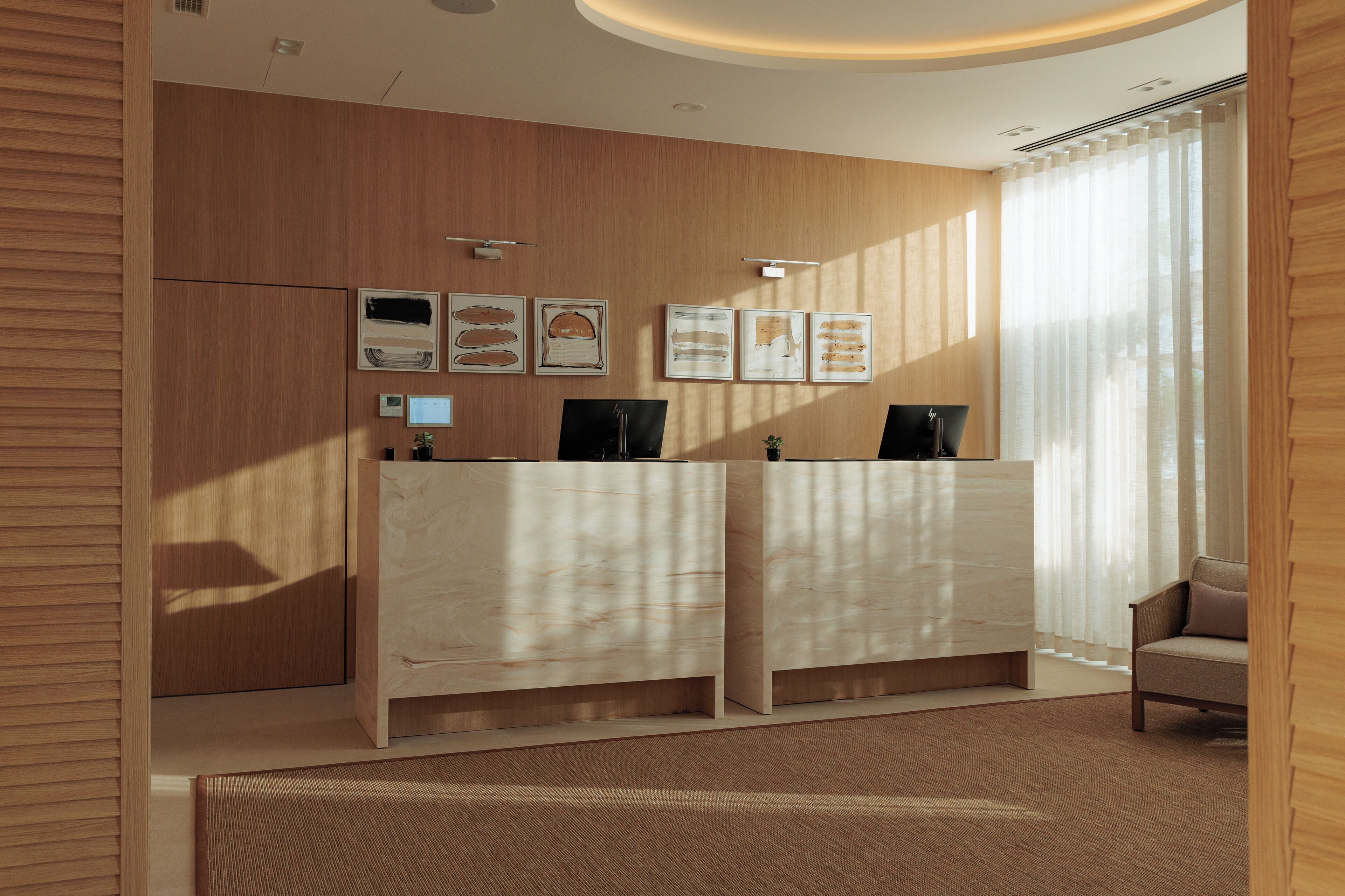A reception area with wooden paneling, a reception desk, framed artwork on the wall, and a window with sheer curtains.