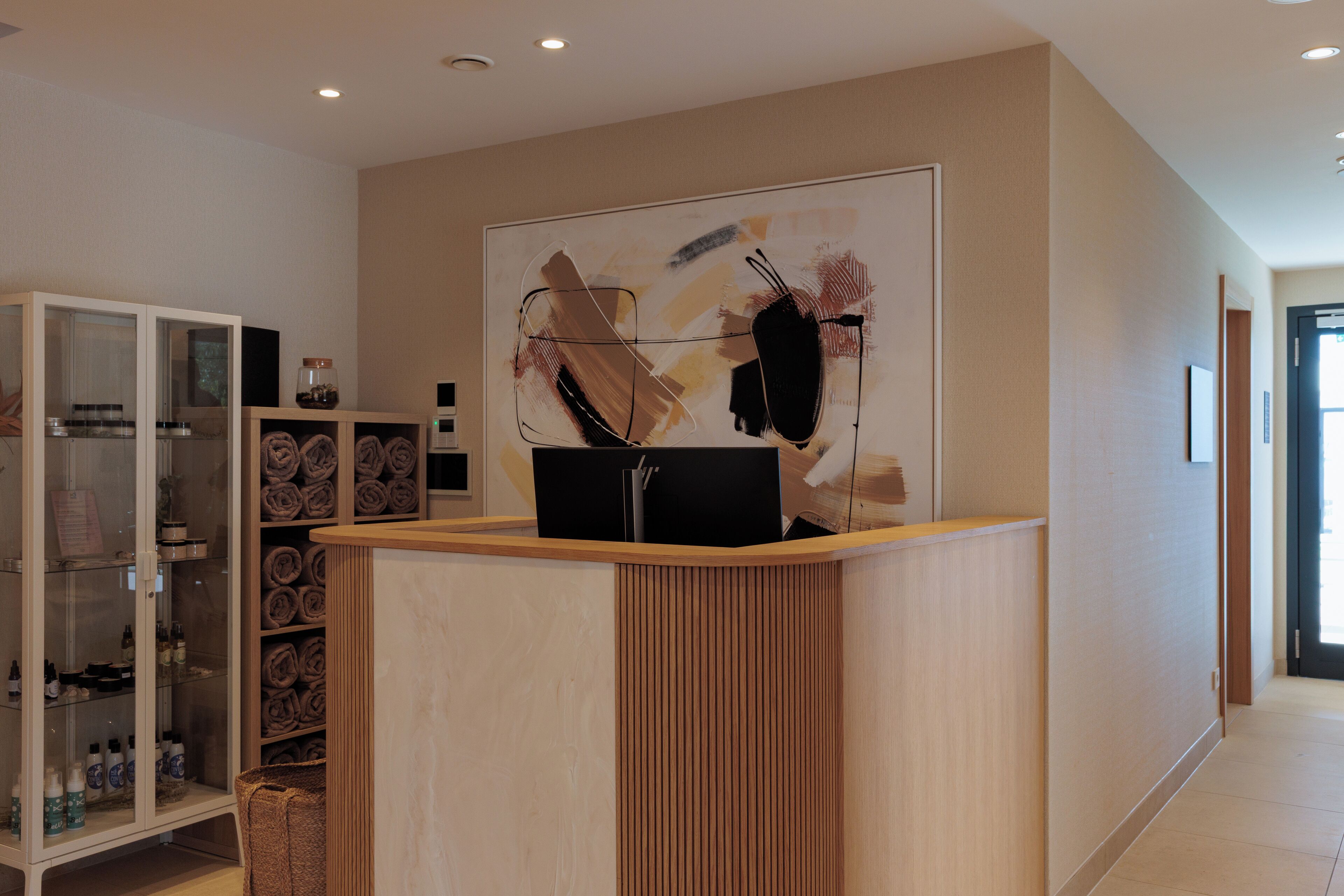 Ein moderner Empfangstresen, eine Vitrine mit Toilettenartikeln und ein großes abstraktes Gemälde an der Wand.