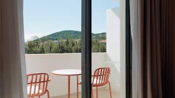 Un balcón con dos sillas naranjas y una pequeña mesa blanca, con vistas a una ladera verde con edificios.