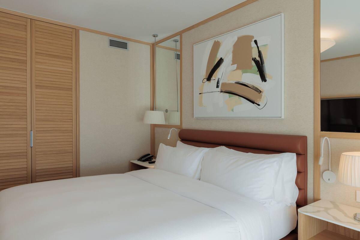 Une chambre d’hôtel avec un grand lit, une armoire en bois, une table de chevet avec une lampe et une œuvre d’art accrochée au mur.