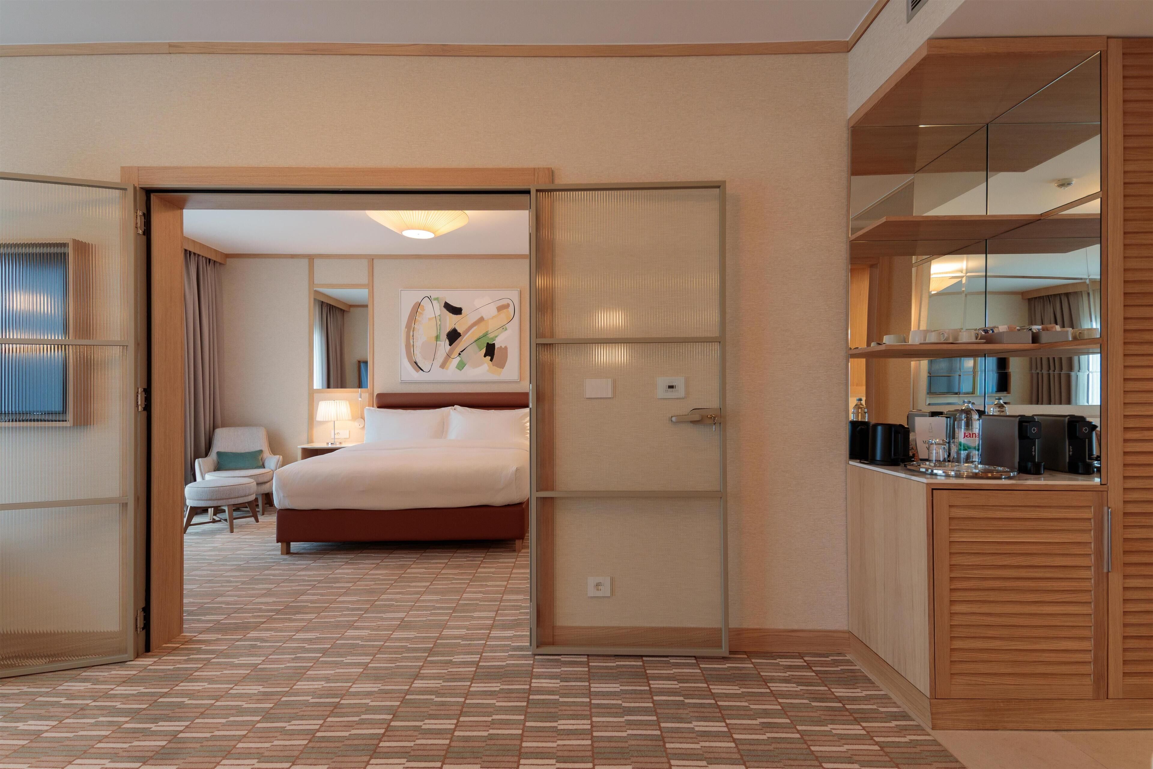 A hotel room with a bed, a desk, a chair, and a kitchenette.