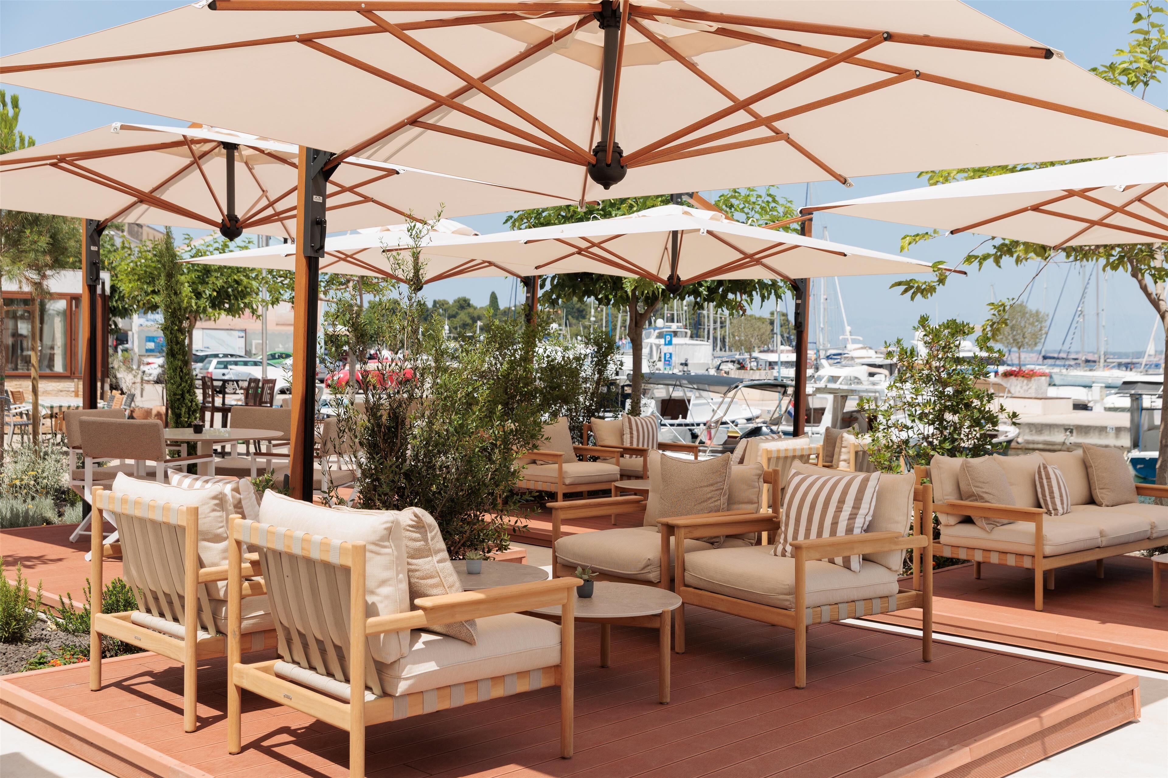 Un espace extérieur aménagé avec du mobilier en bois et de grands parasols, offrant une vue sur une marina où sont amarrés des bateaux.