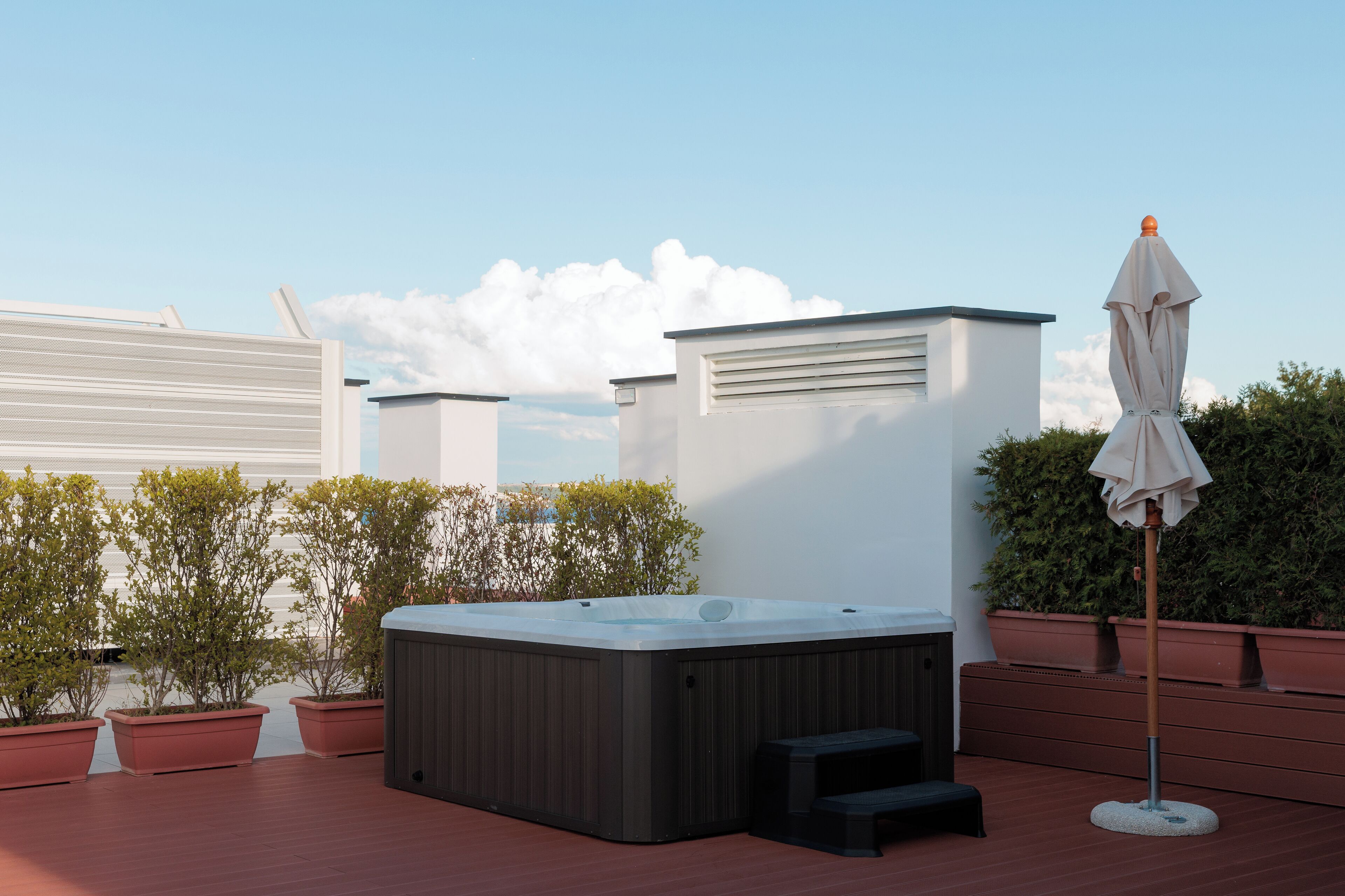 Une terrasse sur le toit équipée d’un jacuzzi, de plantes en pot et d’un parasol.