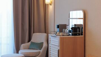 A hotel room with a sofa, a small ottoman, a wooden cabinet with a mirror, and a coffee maker.