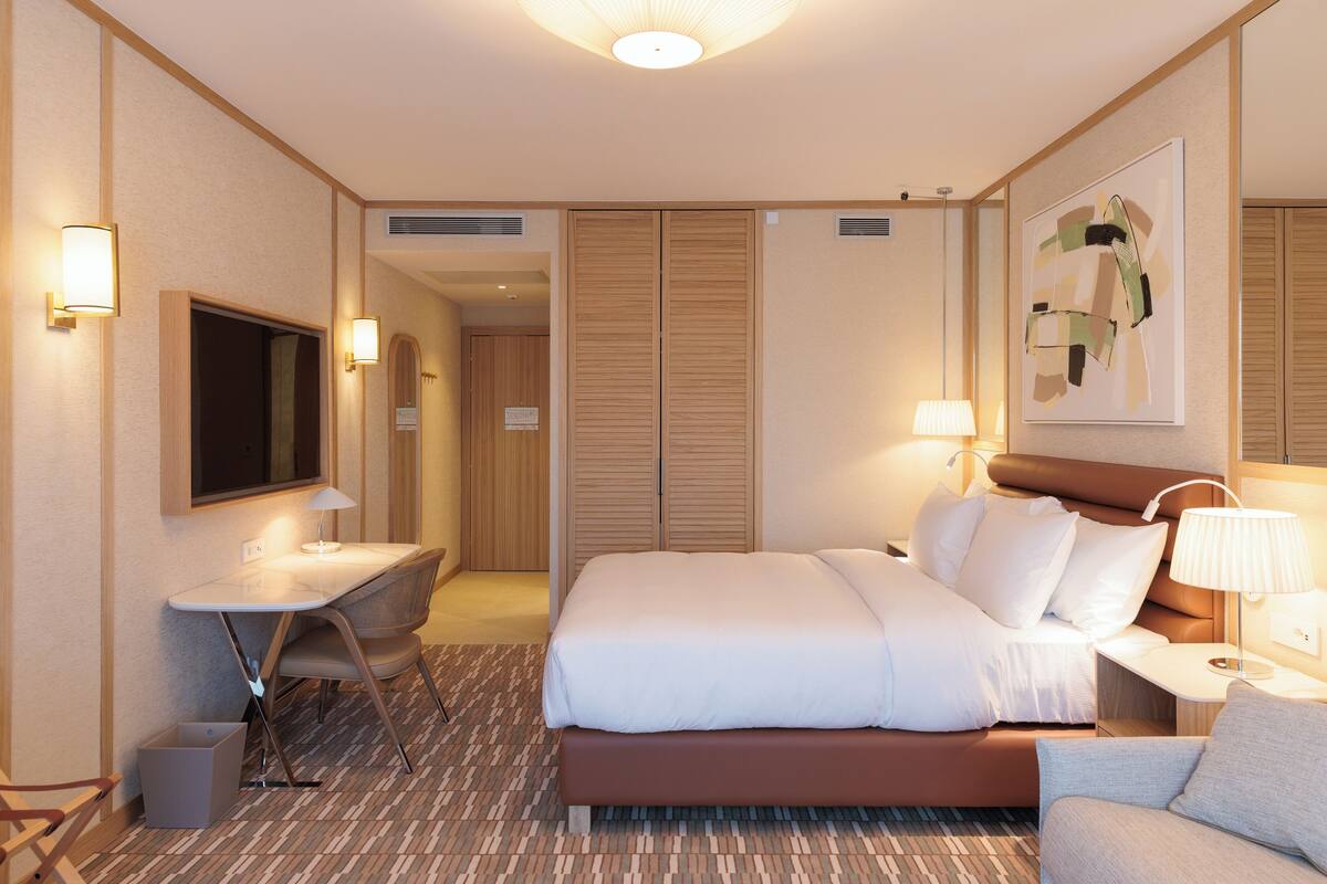 Une chambre d’hôtel avec un lit, un bureau, une chaise, une télévision et un tableau au mur.