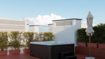 A rooftop with a hot tub, potted plants, and a patio umbrella.