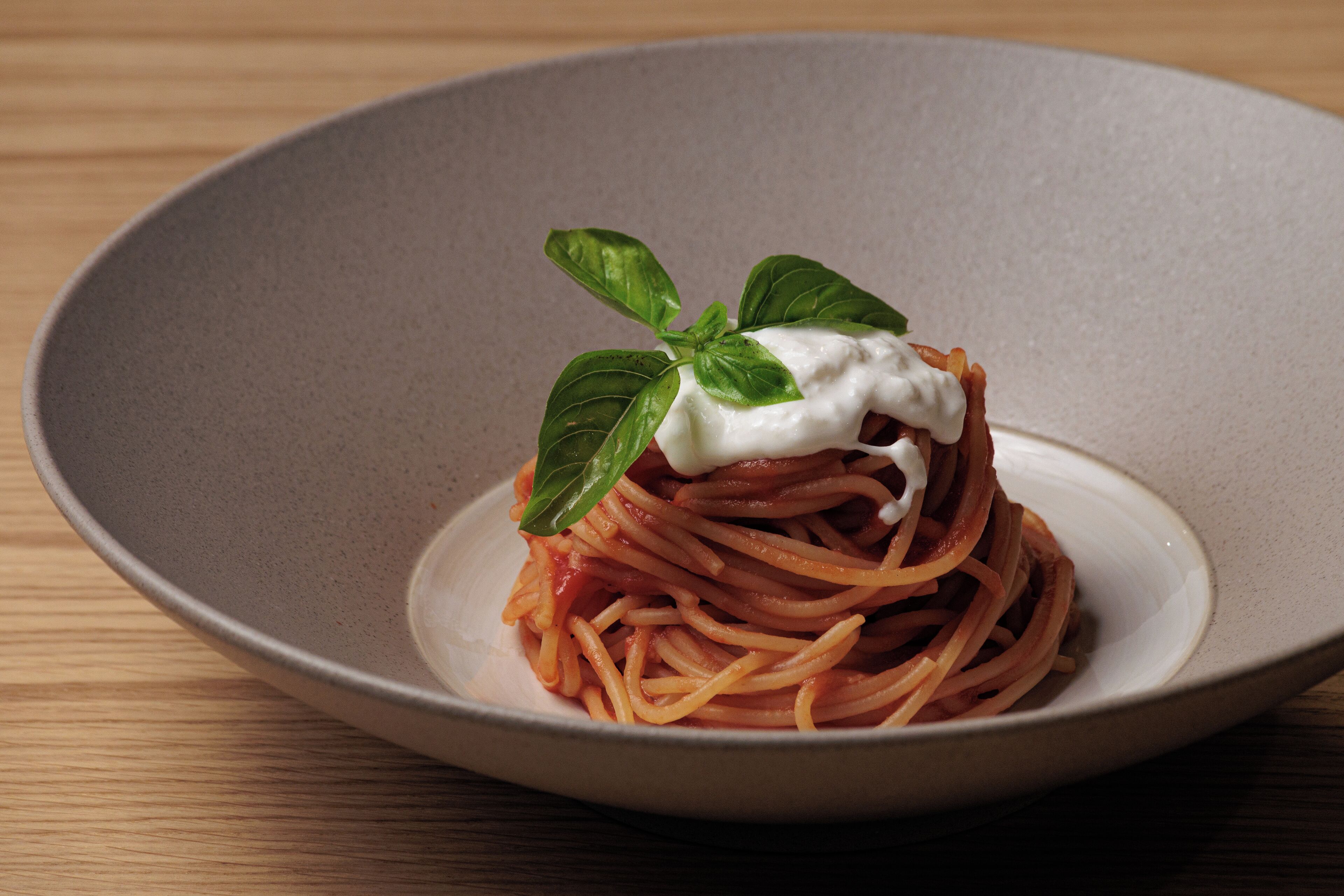A plate of spaghetti with a dollop of cream and a basil leaf on a ceramic plate.