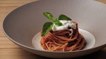 A plate of spaghetti with a dollop of cream and a basil leaf on a ceramic plate.