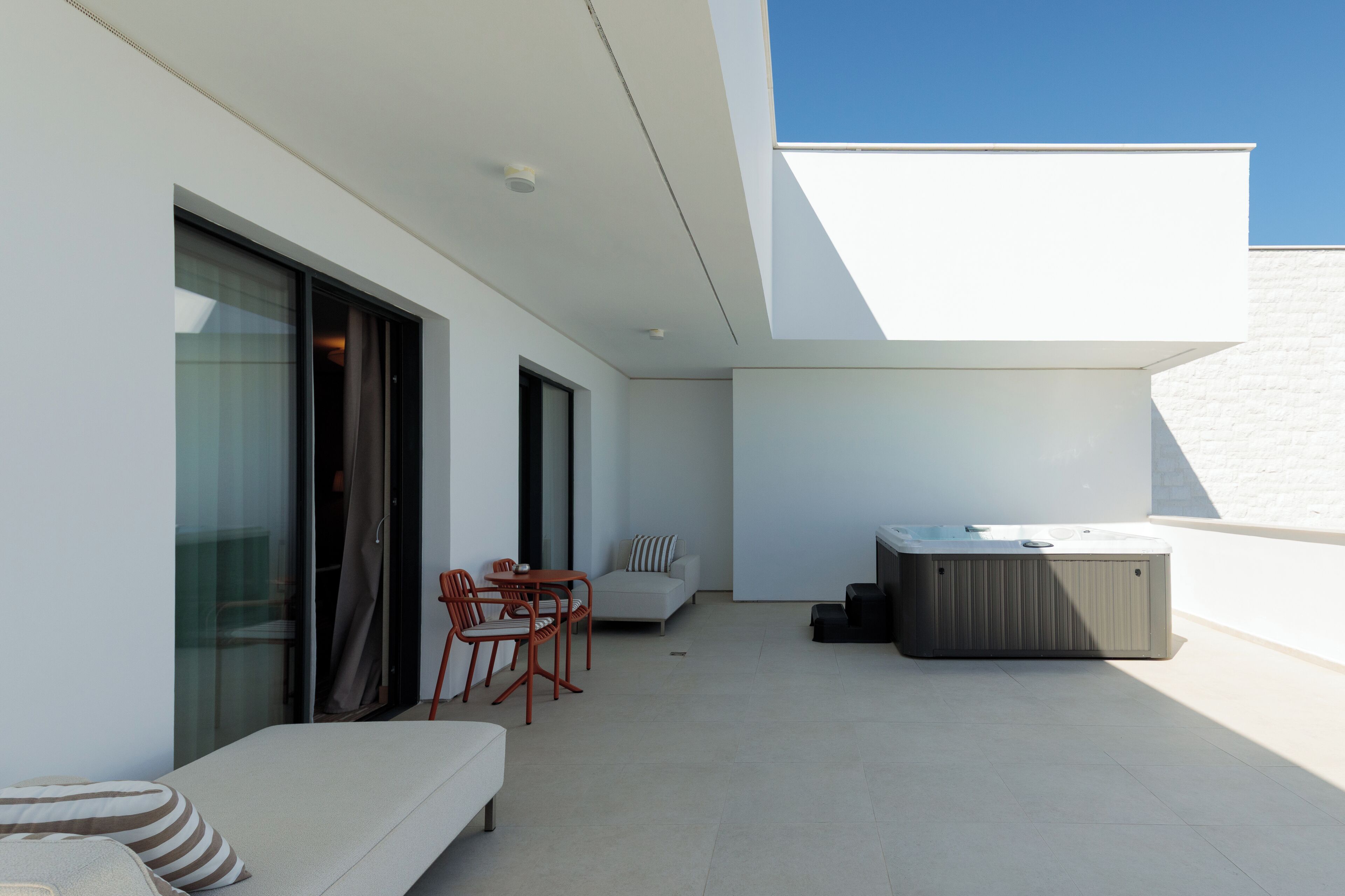 Een modern terras buiten met een bank, stoelen, een tafel en een jacuzzi.