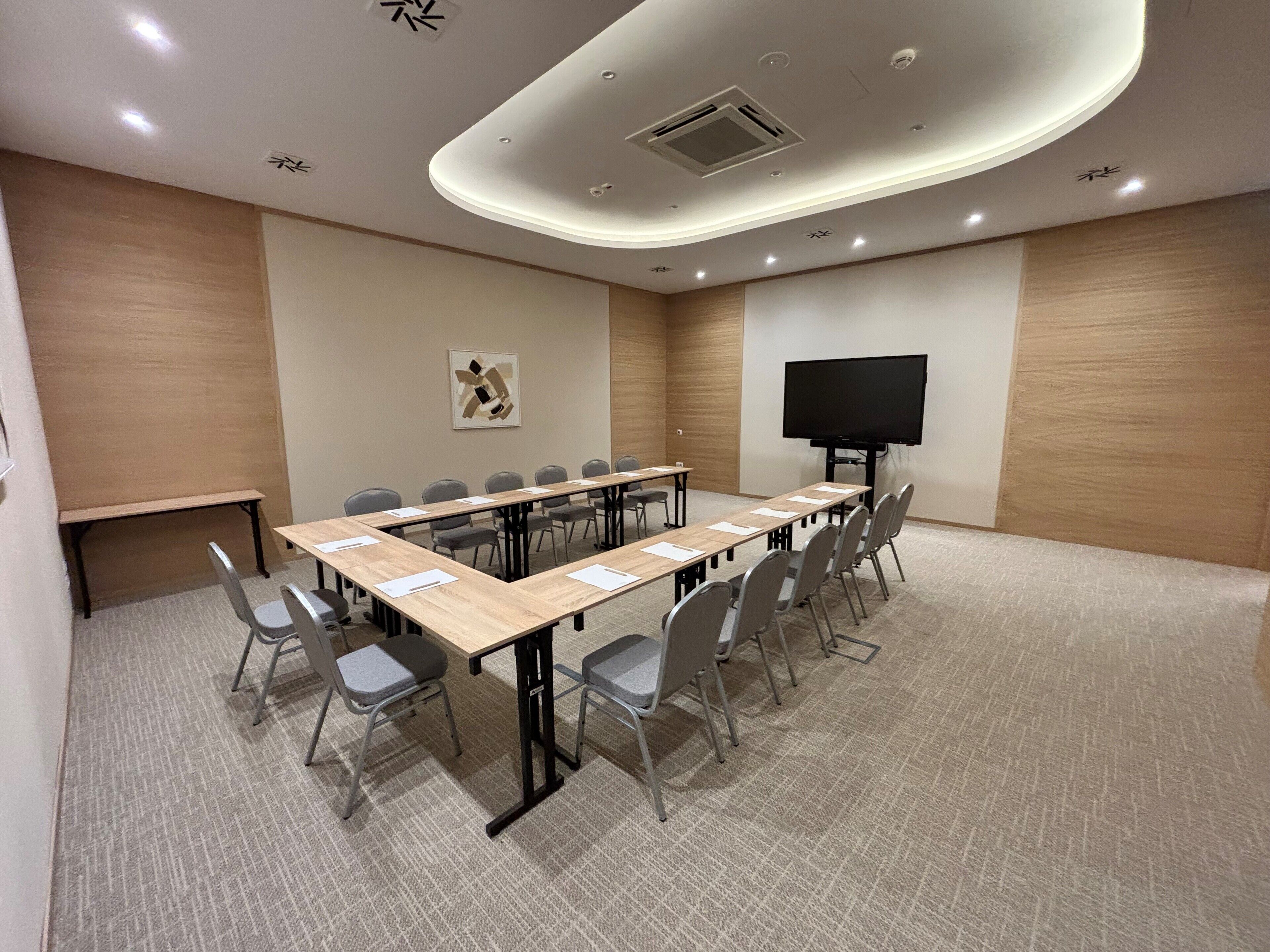 A conference room with a long table, chairs, a TV screen, and a carpeted floor.
