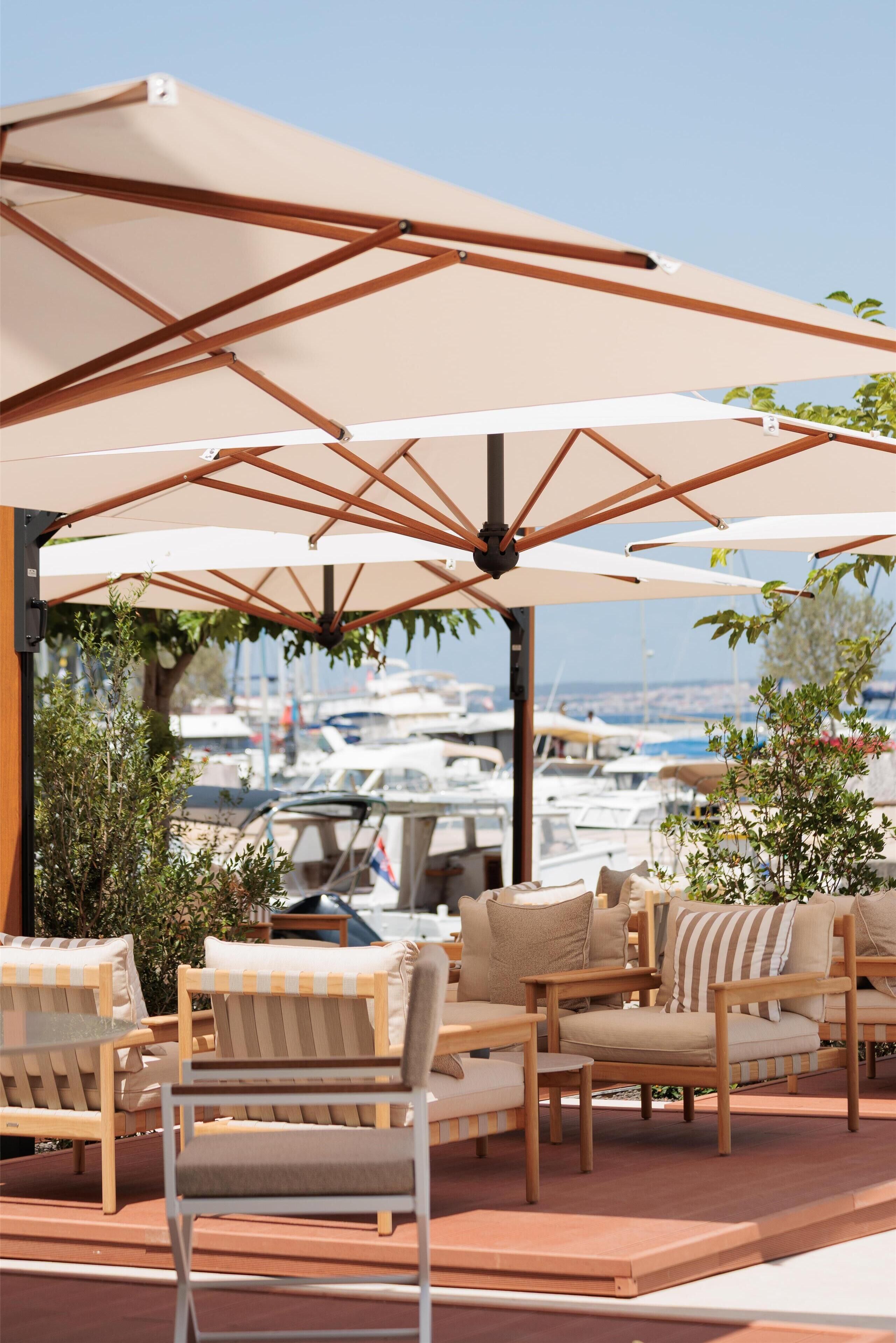 An outdoor seating area with wooden chairs and large umbrellas, overlooking a marina with boats.