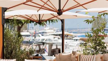 An outdoor seating area with wooden chairs and large umbrellas, overlooking a marina with boats.