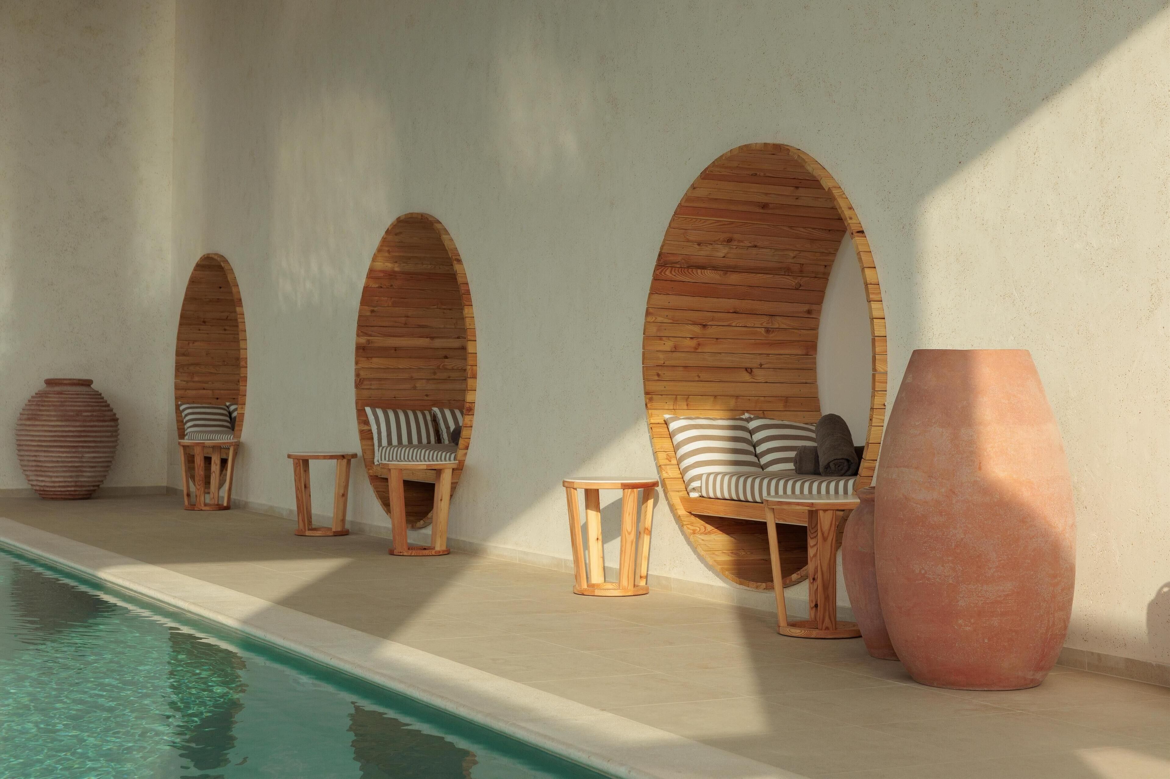 Zona junto a la piscina con arcos de madera, sillones de descanso y una gran maceta de terracota.