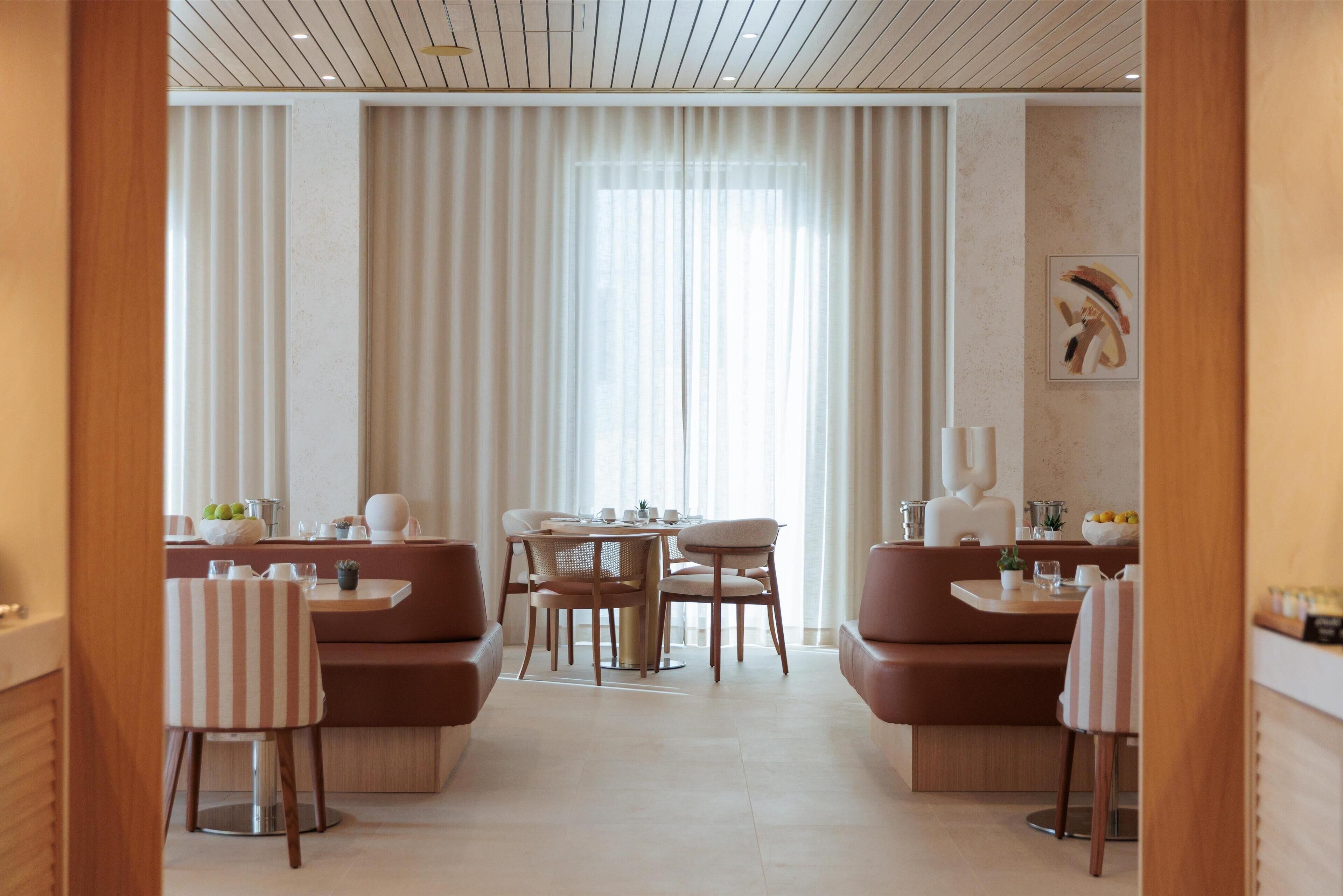 A modern dining area with a round table, cushioned seating, and a large window with sheer curtains.