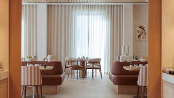 Un comedor moderno con una mesa redonda, asientos acolchados y un amplio ventanal con cortinas translúcidas.