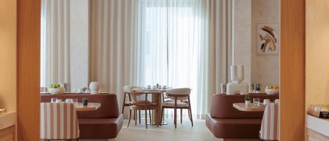 Un comedor moderno con una mesa redonda, asientos acolchados y un amplio ventanal con cortinas translúcidas.