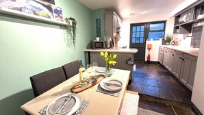 Un coin repas avec une table dressée pour deux personnes, un four à micro-ondes et un réfrigérateur en arrière-plan.