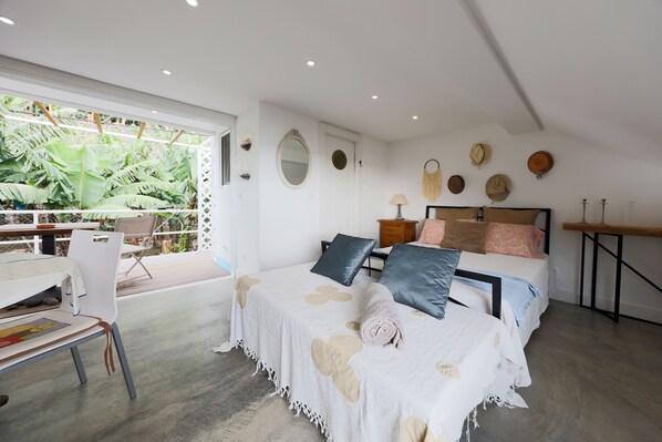 A bedroom with a large window, a bed with multiple pillows, a desk, and a chair.