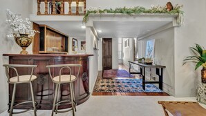 Un vaste espace de vie comprenant un bar en bois, deux tabourets, une table basse et un grand tapis.