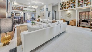 Un salon spacieux avec un canapé blanc, un lustre et une bibliothèque remplie de livres et d’objets décoratifs.
