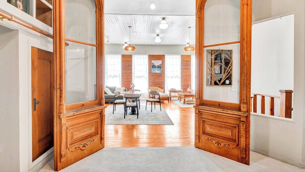 Un salon spacieux avec une grande porte ouverte donnant sur une autre pièce, des meubles en bois et une vue sur la salle à manger.