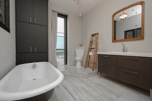 Un baño moderno con una bañera independiente, un espejo grande y una escalera de madera apoyada en la pared.