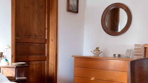 A bedroom with a wooden bed, a dresser, a mirror, and a door. - Montello Hill front property with large garden (Ciano)