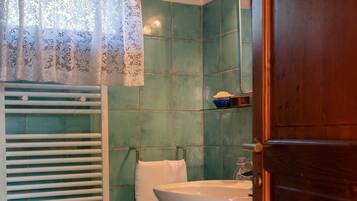 Un bagno con un lavandino bianco, un asciugamano appeso al muro e un tappetino blu sul pavimento.