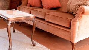 A living room with a brown sofa, a white table, and a lamp. There are three paintings on the wall. - Montello Hill front property with large garden (Ciano)